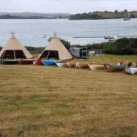 Two small Tipis sit in front of Strangford Lough, Skiffs are lined up in front on the grass