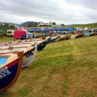 Skiffs are lined up on the grass at Delamont Country Park, two Tipis are in the distance