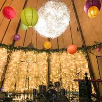 A Tipi is dressed for a birthdy party with fairlight panels, foliage and colourful paper lanterns hanging from the roof
