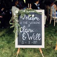 A blackboard on an easel, decorated in foliage welcomes guests to a wedding