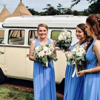 Three bridesmaid stand in front of a vintage cream volkswagen van, three tipis stand behind it