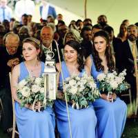 Three bridesmaids dressed in blue sit during the ceremony holding bouquets, the wedding guests sit behind them