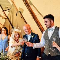 The wedding party cheers and clink glasses inside a Tipi Wedding