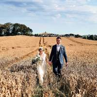 The bride and groom hold hands as they walk through a wheat field together
