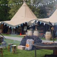 BBQ's and grills are smoking and cooking meats with two Festival Tipis standing behind them
