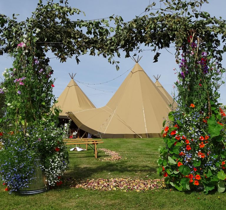 Three tipi wedding setup in an open field with a beautiful DIY floral square arch