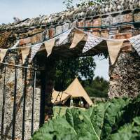 Wedding tipi captured through a walled archway decorated with bunting