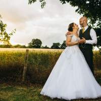 Bride and Groom look at eachother holding hands in front of wheat field highlighted by a beautiful sunset glow