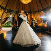 The Bride and Groom have their first dance inside a tipi decorated with guests and band in the background