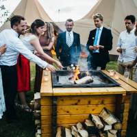 Cheerful wedding guests surround magnakatas firepit with drinks in hand and toasting marshmallows