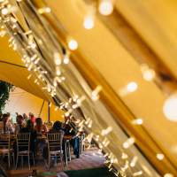 Fairylit panels decorate inside one of magnakatas wedding tipis with guests seated in the background