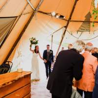 The bride lifts her bouquet as she walks with the groom into their tipi wedding reception