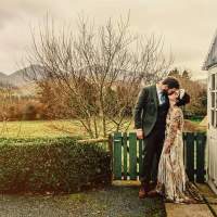 The bride and groom kiss in front of an outhouse, the Mourne Mountains sit in the background
