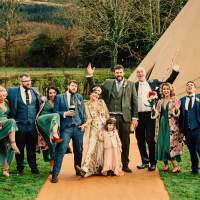 The wedding party pose for a fun photograph in front of a wedding tipi