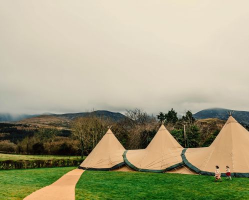 Three Tipis are setup in a field with beautiful irish countryside in the background