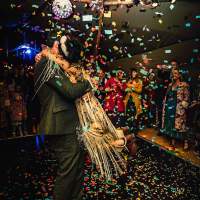 The groom swings the bride around on the dancefloor, coloured confetti falls around them