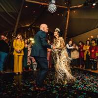 The bride dances with her father in a gorgeous embroidered fringe dress surrounded by guests inside their wedding tipi