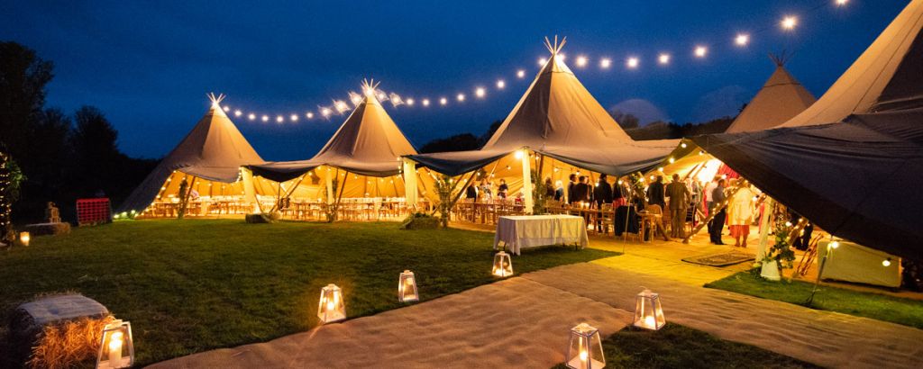 Gorgeous six tipi set up in an arc with open sides , festoon lights and a lit up entrance walkway