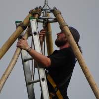 A magnakata crew member is on a ladder fitting the central tipi wooden poles together