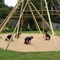 Six Magnakata crew work together to nail down matting at the base of three tipis in a walled garden