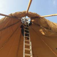 A Magnakata crew member is on a ladder fixing the Tipi canvas in place at the central poles
