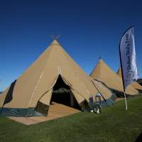 Three Tipis are joined in a row on green grass, Dubai Duty Free flags stand either side of the entrance
