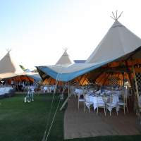 Three joined Tipis with open sides show formal dining chairs and tables waiting for corporate guests to arrive