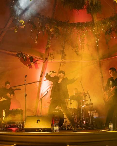 A band is lit up with warm yellow uplighters on a Magnakata stage at Tipi Party