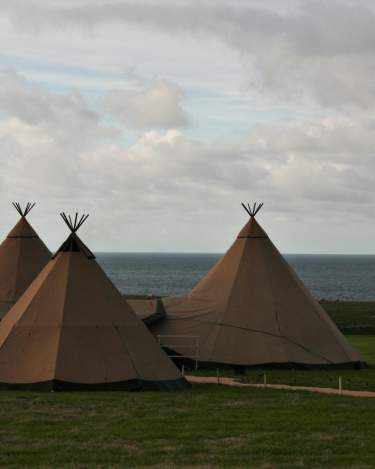 Four Tipis are joined together, overlapping canvases and festoon lighting, a bright blue cloudy sky is in the background