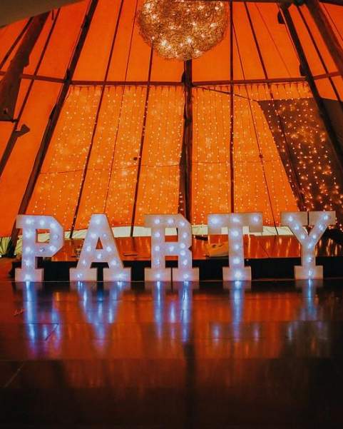 Large Lettered Lights spelling out Party stand in front of staging inside a tipi