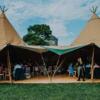 Open sided entrance to a five tipi wedding reception, inside is crowded with guests sitting at tables