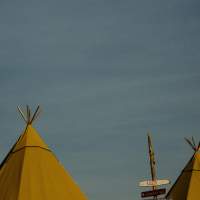 Three tipi tops at sunset, warm blue skies and tree tops stand behind them