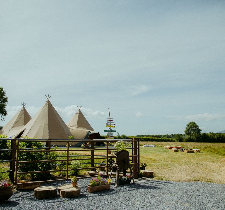 Three tipi wedding in a field, with a handmade wooden signpost and metal fencing in front