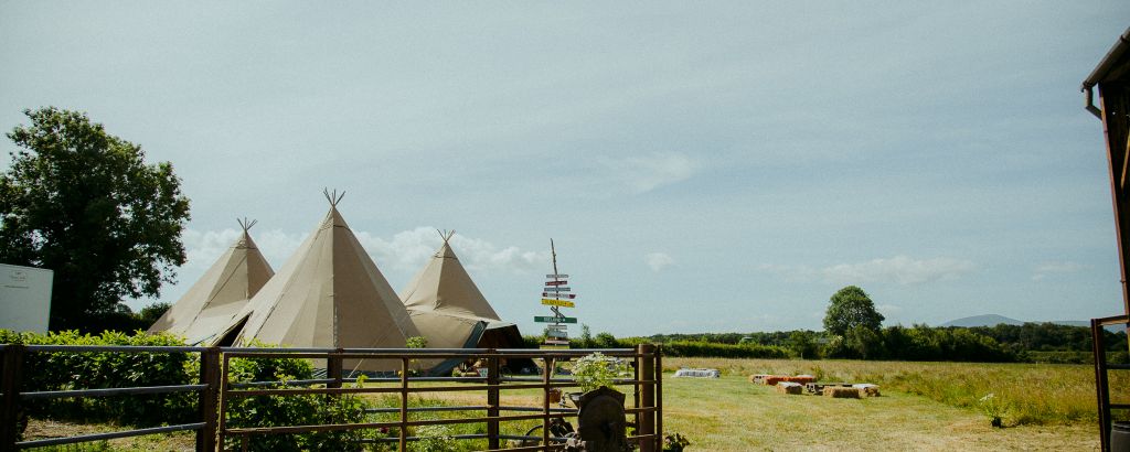 Three tipi wedding in a field, with a handmade wooden signpost and metal fencing in front