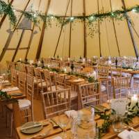 Inside a tipi is decorated with green foliage and candles on top of long rows of wooden tables