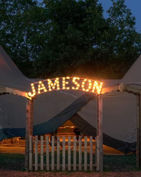 A two tipi set up with Jameson circus light style arch entrance at night